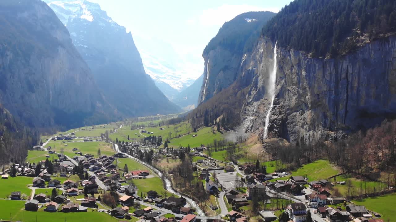 Aerial drone view showcases small village nestled amidst majestic cliffs during daytime in Switzerland, highlighting stunning contrast between quaint homes and towering rocky formations