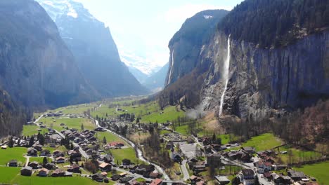 aerial drone view showcases small village nestled amidst majestic cliffs during daytime in switzerland, highlighting stunning contrast between quaint homes and towering rocky formations