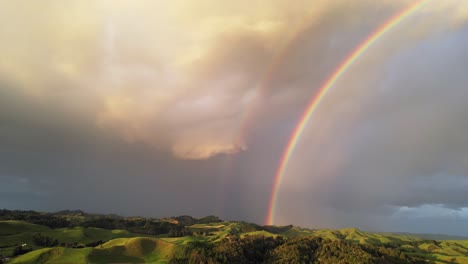 Doppelter-Regenbogen-Im-Dunklen-Himmel-über-Grünen-Hügeln-In-Neuseeland