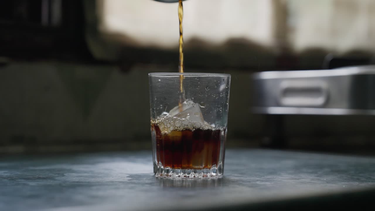 A close-up, slow-motion of pouring black tea into a glass cup with ice cubes against a blurred background