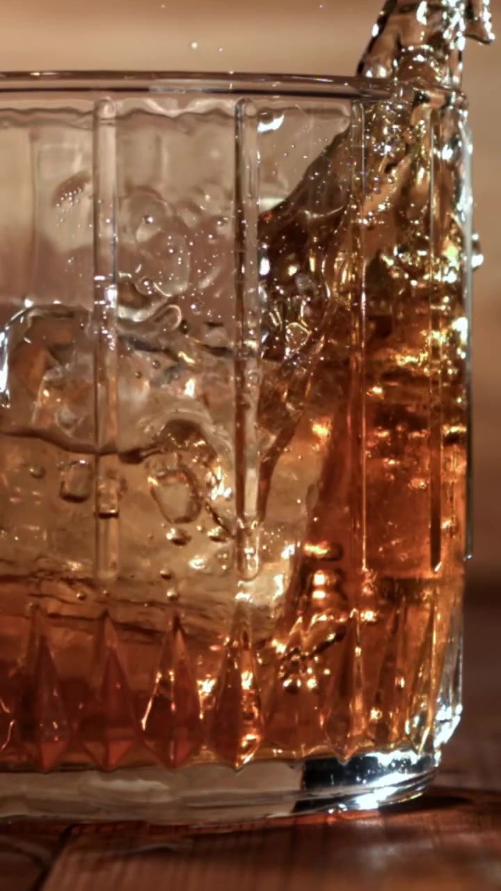 Versare whisky con cubetti di ghiaccio in un bicchiere al rallentatore