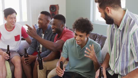 happy diverse male friends talking and drinking beer in living room