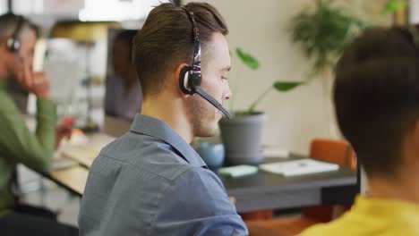 Portrait-of-happy-caucasian-businessman-using-phone-headset-and-looking-at-camera-at-office