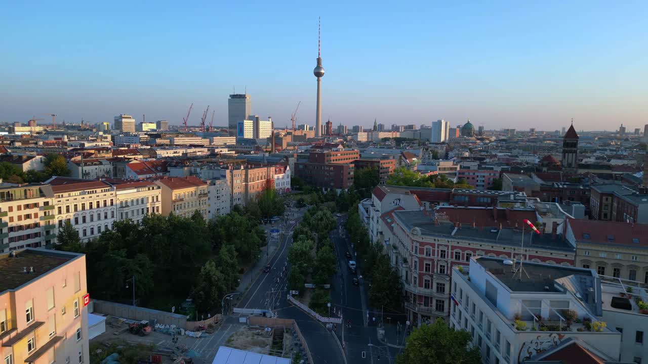Berlin tv tower rising above rooftops and a construction site at senefelderplatz during sunset. Majestic aerial view flight fly reverse drone
