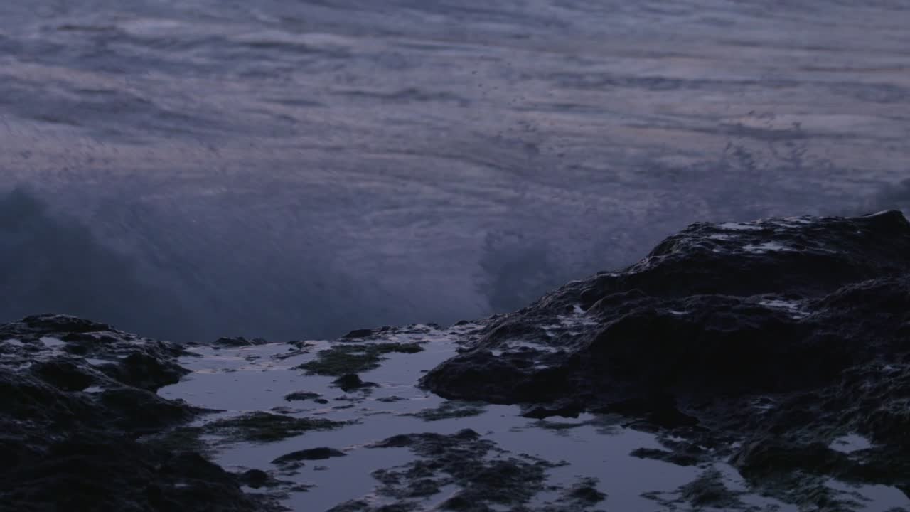Close-up: Wave washes over rocky tide pool. Filmed at sunset on the Oregon Coast.