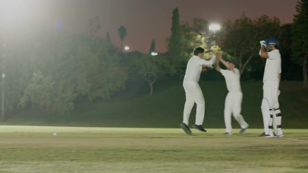 Cricket højrehåndsbowler bowler på oplyst bane, holdet spurter og appellerer for wicket midt i forstyrrelser