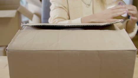 young caucasian lady closing cardboard parcel and preparing it