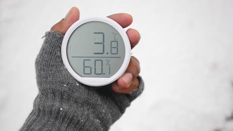 handheld digital thermometer showing 3.8°c and 60% humidity in snow