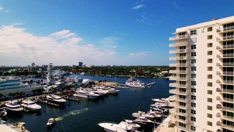 nice aerial shot of yachts and boats in the water flying past a building blue sky white clouds ft