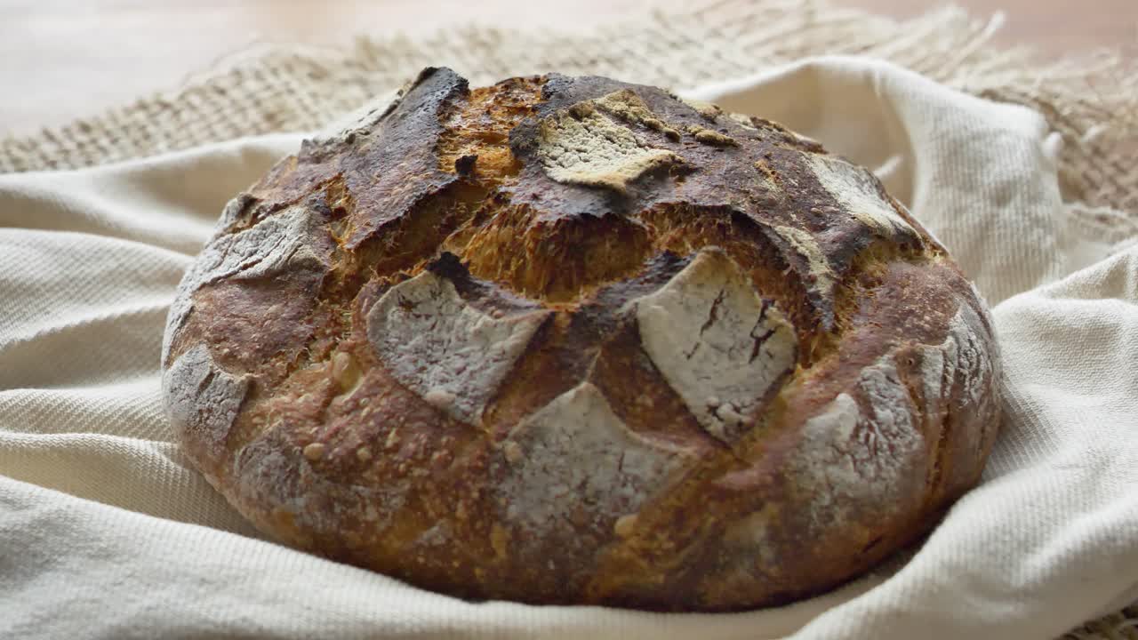 4K video of homemade sourdough bread loaf rotating from right to left on linen. Rustic artisan food shot, perfect for bakery, cooking, and culinary projects