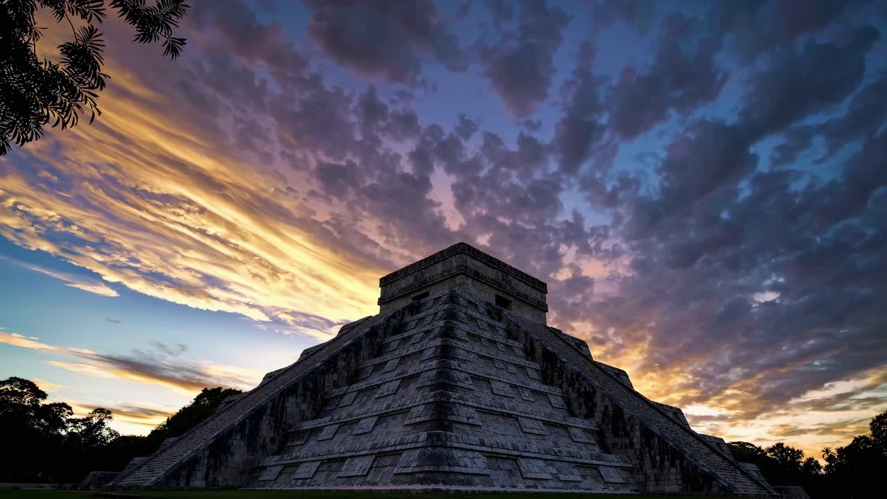 Low-angle shot of an ancient pyramid at sunset, capturing dramatic clouds and vibrant colors