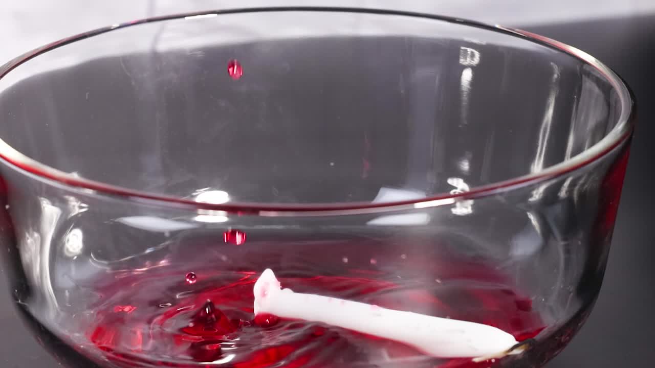 A glass cylinder displaces red liquid in a transparent bowl, demonstrating fluid interaction.