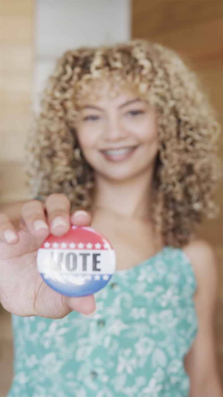 Vertical video: Young biracial woman holding up VOTE badge, smiling