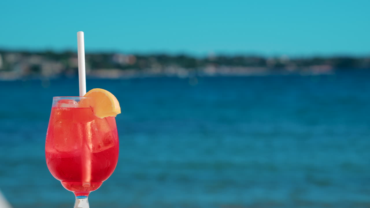 Refreshing red orange cocktail with ice and orange slice against the deep blue Mediterranean Sea