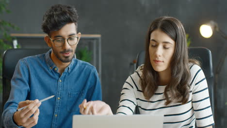 Hombre-árabe-Y-Mujer-Morena-Sentados-En-El-Escritorio-Juntos-Y-Trabajando-Frente-A-La-Computadora-Portátil-En-La-Oficina