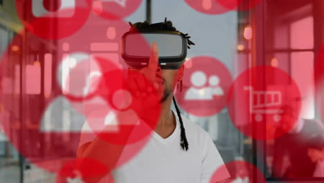 iconos digitales rojos flotando contra un hombre de negocios afroamericano que usa auriculares vr en casa