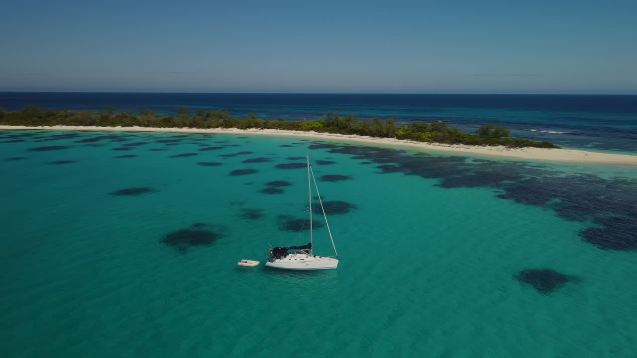 paralaje aéreo alrededor de un velero anclado en una cala tranquila frente a una isla pequeña, isla de pinos