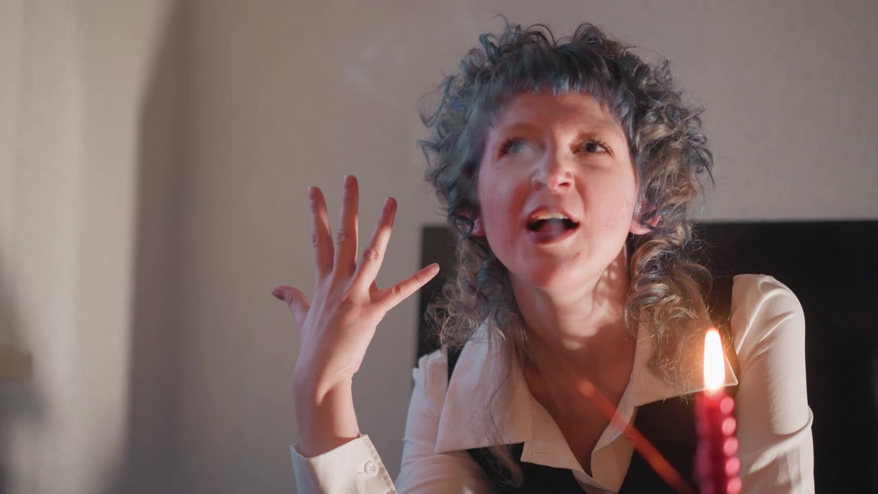 Mulher cacheada realizando ritual de vela com foco em gesto de close-up e respiração criando fumaça, movimento do pulso, chama bruxuleante, atmosfera tensa, profecia expressiva e charme teatral.