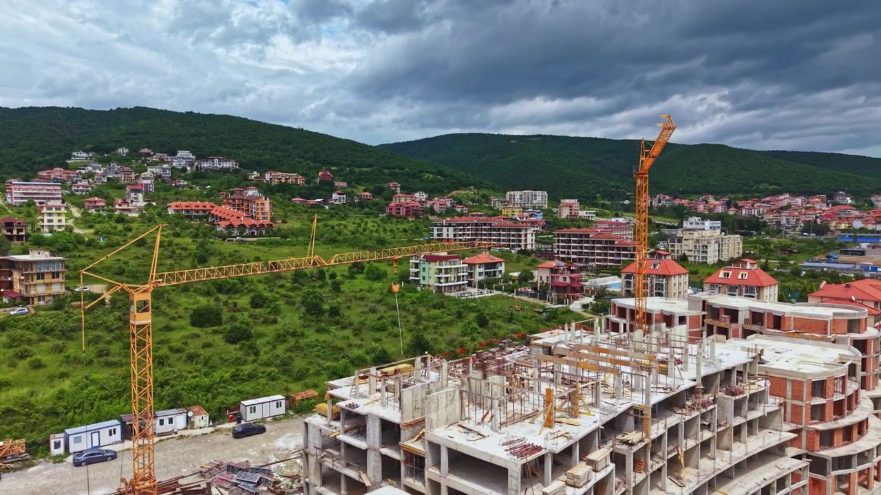 Tháp cẩu giám sát khu dân cư và thương mại đang mở rộng ở vùng nông thôn. Quang cảnh trên cao của khu vực xây dựng đang phát triển với cần cẩu và những ngôi nhà hiện đại dưới nền trời nhiều mây.
