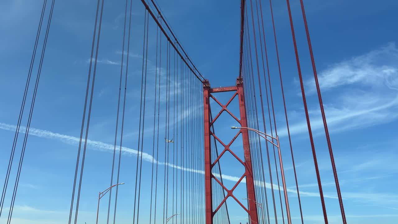 Airplane Flying Over Red Suspension Bridge Against Blue Sky