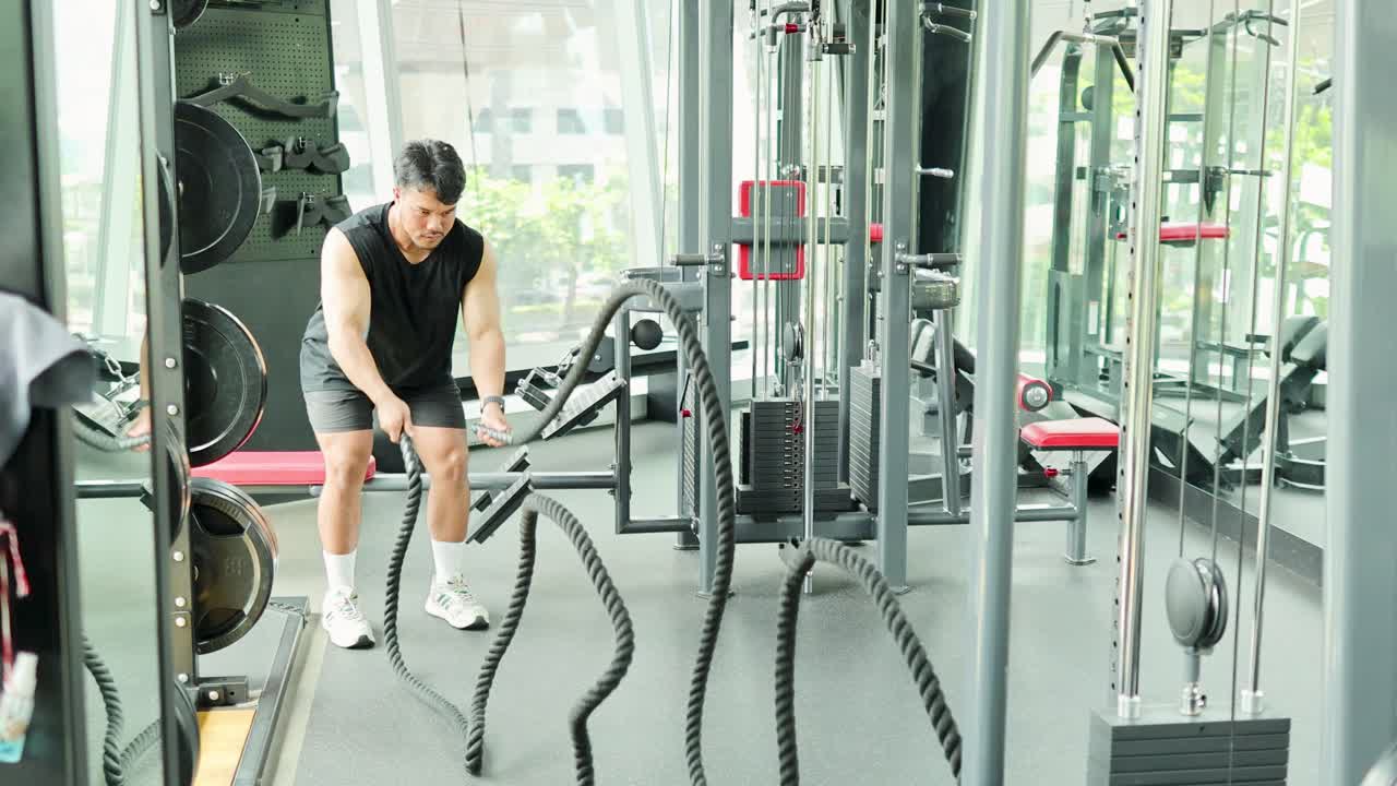 A person performs tricep rope pulldowns in a well-lit Bangkok gym, showcasing strength and focus during a crossfit workout