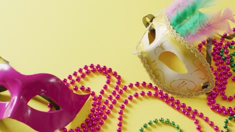 video of two masquerade masks and carnival mardi gras beads on yellow background with copy space