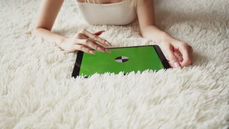 la mujer está acostada en la cama y usando una tableta electrónica con pantalla verde, vista superior. las manos femeninas usan una tableta digital. maqueta, primer plano. concepto de uso de aparatos digitales