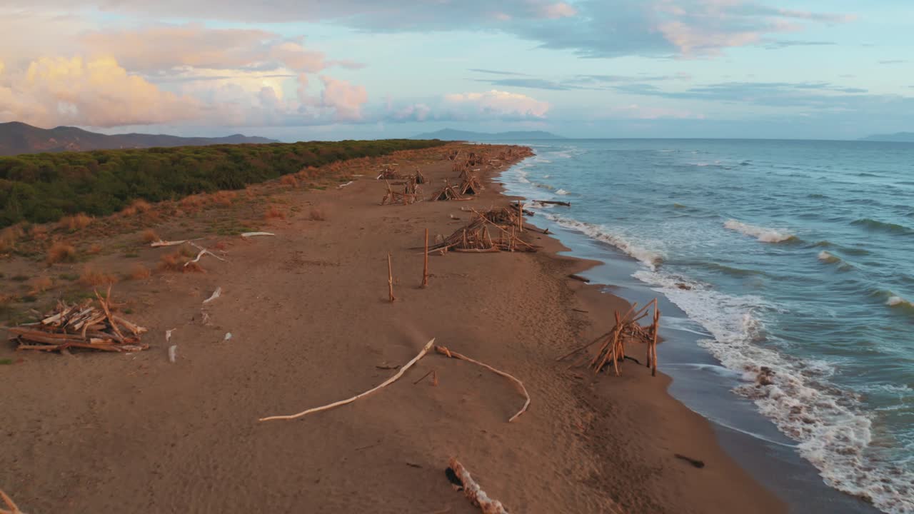 кадры с воздуха соснового леса и песчаного пляжа на берегу моря в легендарном природном парке маремма в тоскане, италия, с драматическим облачным небом на закате и деревянными типи вдоль пляжа