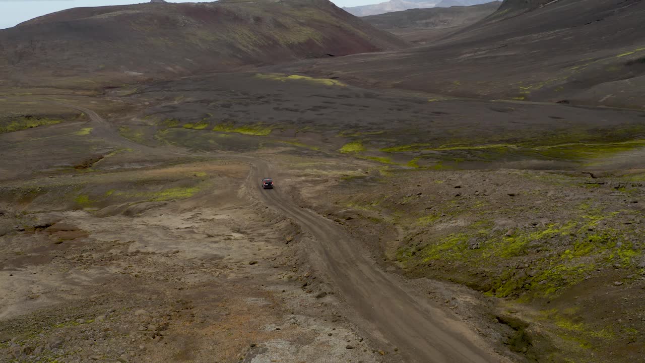 Vista aerea di una strada sterrata tortuosa attraverso un terreno vulcanico scuro con chiazze sparse di muschio verde negli altopiani islandesi