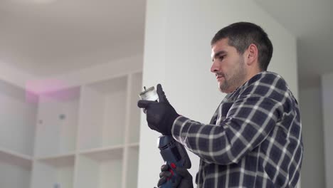 a carpenter with a circular drill drilling holes in the kitchen shelves.
