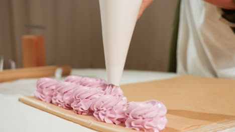 close up of cupcake preparation showing piping bag forming swirls of fluffy pink dough on brown baking paper in neat row during baking process inside cozy kitchen with soft lighting and rustic decor