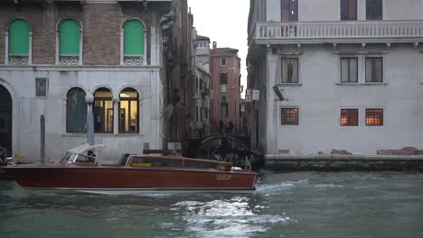 A-canal-intersection-in-Venice,-typical-Venetian-houses,-a-vaporetto-taxi-passing-through-the-canal-and-crossing-paths-with-a-bird