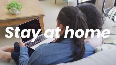 animation of stay at home text over biracial couple using laptop