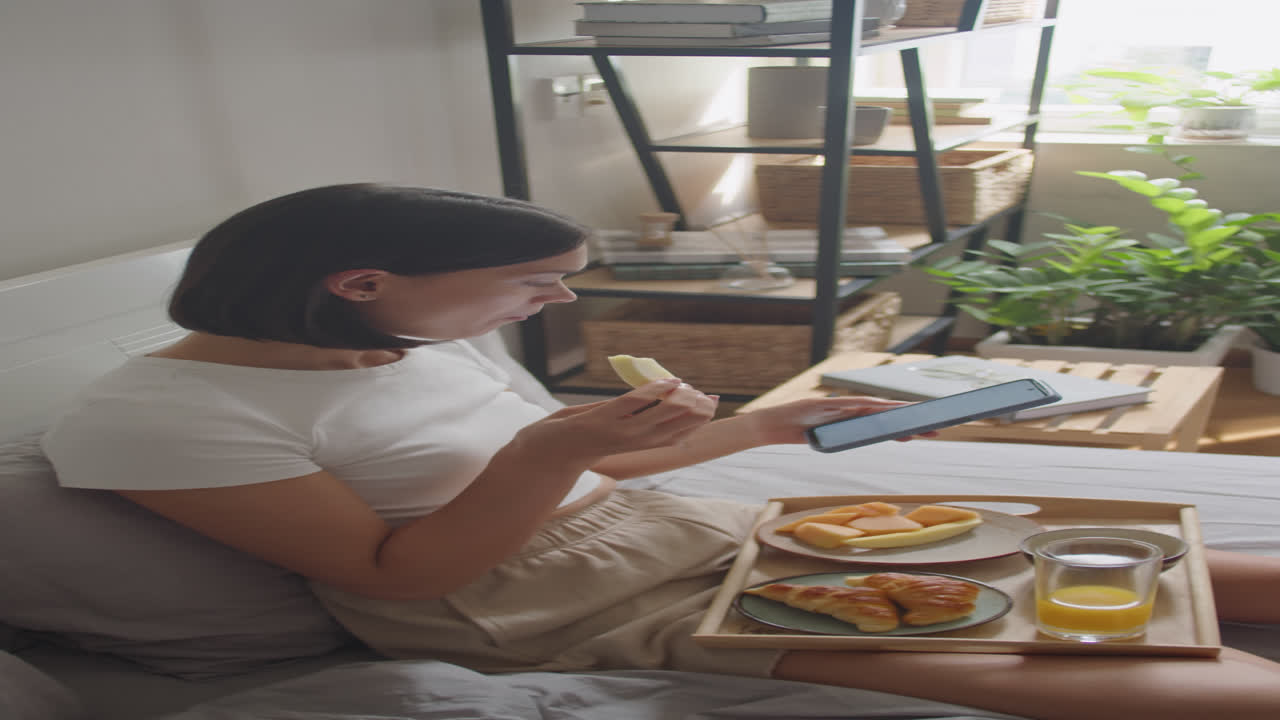 Woman Having Breakfast in Bed and Scrolling on Phone