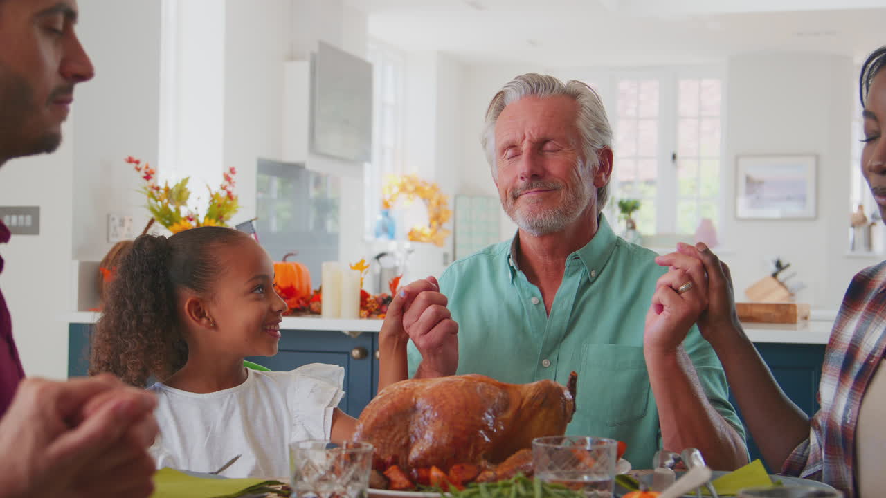 Grand-père parlant à sa petite-fille tandis que la famille multi-générationnelle prie avant le repas de Thanksgiving
