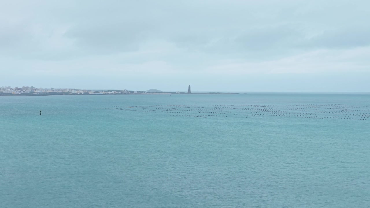 Wide drone shot of the calm Taiwan Strait open seawater with distant oyster farm industrial activities of Penghu Islands under cloudy sky, Penghu County, Taiwan