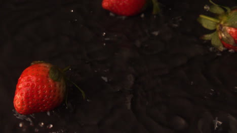 Strawberries-falling-on-wet-black-surface