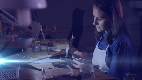 animation of glowing light over caucasian woman using tools working in workshop