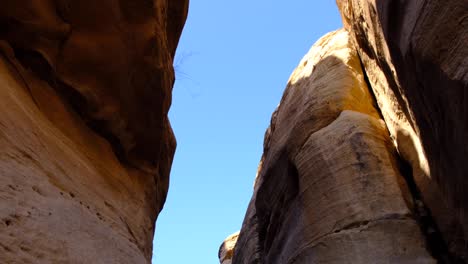 looking up at steep, craggy red rock formations at sunny blue sky deep within valley in the desert wilderness of wadi ghuweir in jordan, middle east