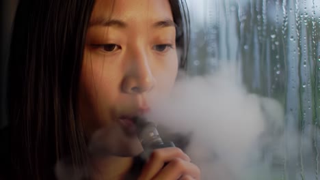 a young woman reflects while vaping near a rainy window, capturing a moment of contemplation and serenity amidst the drizzling environment