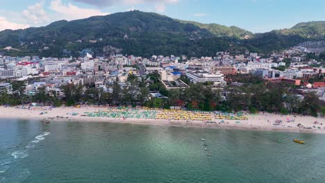 drone footage captures patong beach's vibrant shoreline and bustling cityscape under clear skies, showcasing the lively atmosphere of phuket, thailand