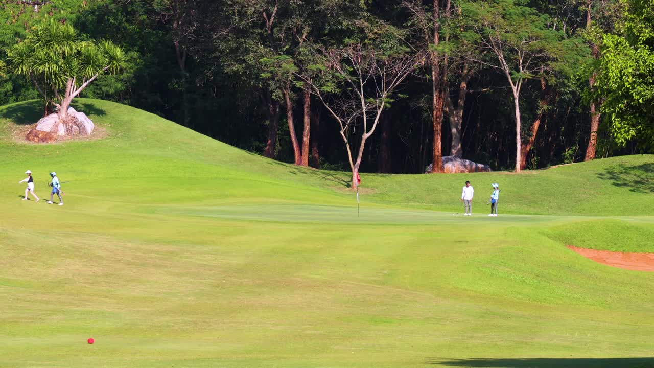 Golfers and caddies walk along green fairway, bright sunlight, wide shot, slow camera pan