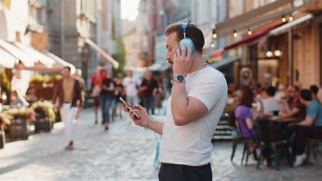 happy young man in wireless headphones choosing listening music in smartphone dancing outdoors