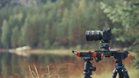 a professional camera on the slider rig stands on the bank of the shallow lake