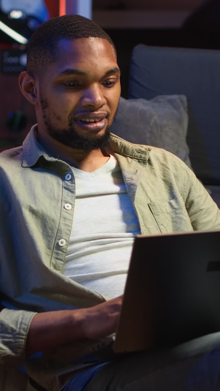 Vertical Video Adult guy typing on laptop laying on couch at his stylish loft space
