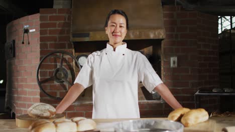 animation of happy asian female baker smiling at camera in bakery