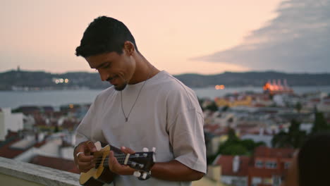 Signing-man-relax-balcony-on-weekend-holiday.-Carefree-guy-play-ukulele-guitar