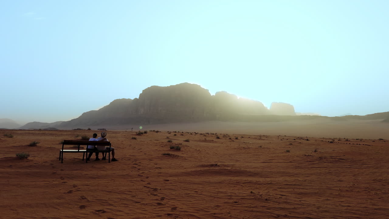 해가 뜨는 와디 럼 사막 의 벤치 에 앉아 있는 두 사람