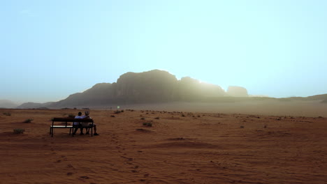 dos personas sentadas en un banco en el desierto de wadi rum al amanecer