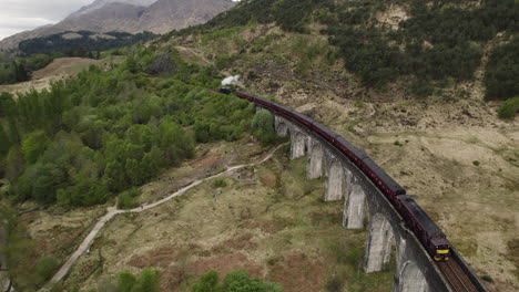 Luftaufnahme-Des-Jacobite-Dampfzuges,-Der-über-Das-Glenfinnan-Viadukt-Fährt,-Mit-Weißem-Dampf,-Der-Von-Hinten-Folgt,-Schottland